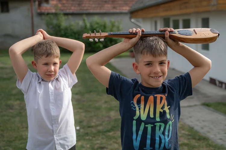 Két fiú áll az udvaron, egyikük tamburát tart a feje fölött, miközben a másik összekulcsolja a kezét.