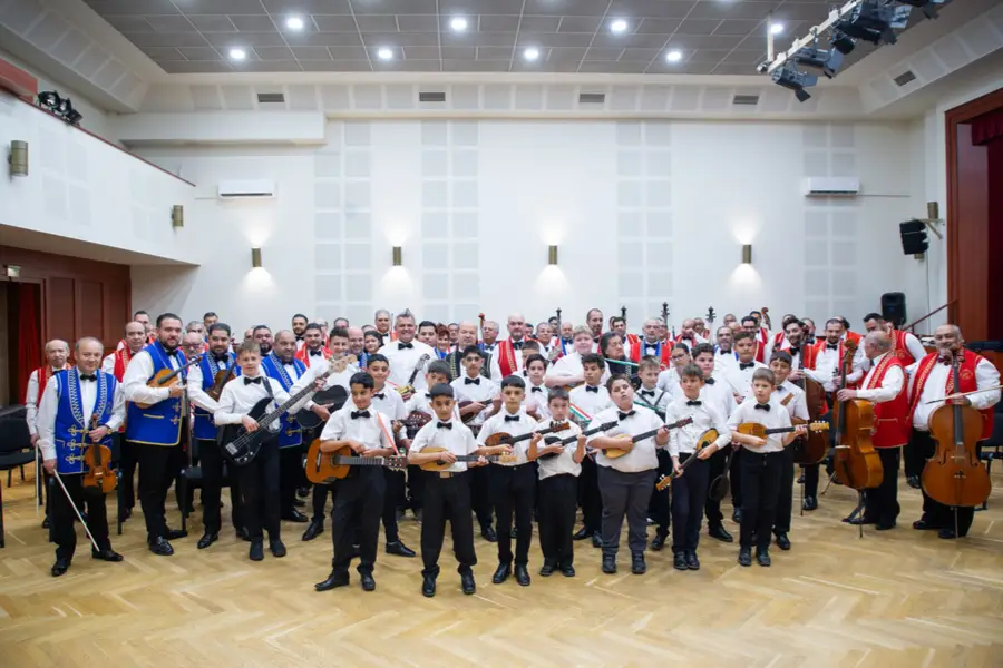 A SUGO Tamburazenekar gyermekei és a 100 Tagú Cigányzenekar közös csoportképen állnak hangszereikkel.
