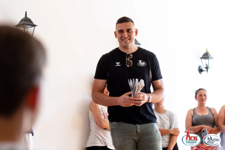 PICK Szeged játékos jegyeket tart a kezében, mögötte gyerekek ülnek a teremben