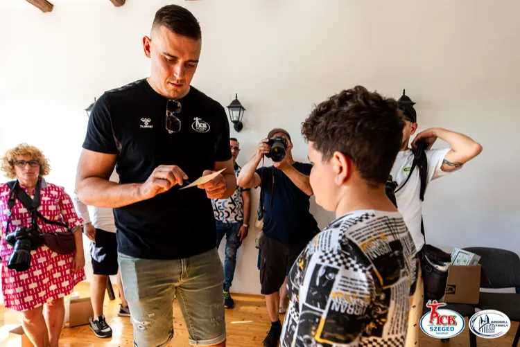 PICK Szeged játékos autogramot ír egy fiúnak, miközben fotósok figyelik az eseményt