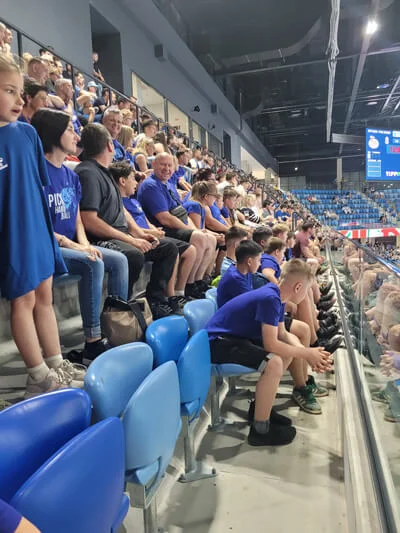 Gyerekek és felnőttek sorakoznak a PICK Aréna lelátóján, miközben a pálya felé fordulva szurkolnak.