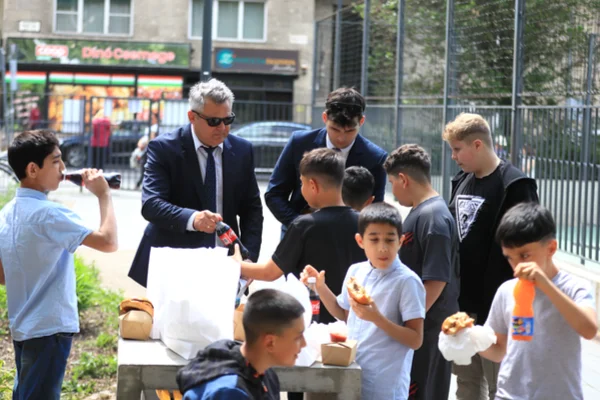 A zenekar vezetője italt ad egy fiúnak, miközben a gyerekek hamburgereznek a Szent István parkban.