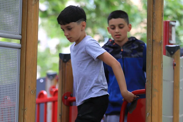 Két fiú halad lefelé a játszótéri mászókáról, miközben a többiek a háttérben játszanak.