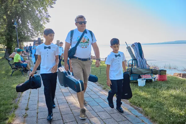 SUGO tamburások hangszertokokkal sétálnak a Balaton-parton a Duna TV révfülöpi adása előtt.