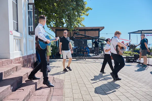 Fehér inges tamburások hangszerekkel mennek a szabadtéri színpad felé a Balaton-parton.