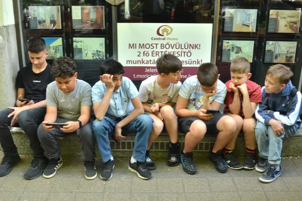 A Sugó Tamburazenekar fiútagjai egymás mellett ülve pihennek, többen a telefonjukat nézik.