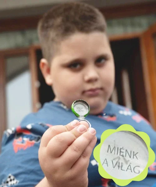 Fiú közelről mutat egy „Miénk a világ” feliratú TopJoy kupakot, amelyet úton az Országházba talált.