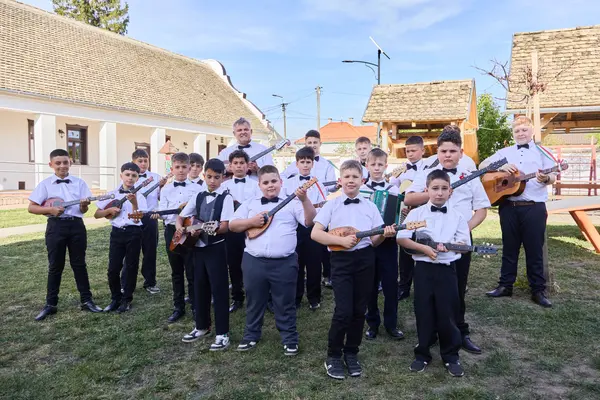 A SUGO Tamburazenekar gyermekei hangszereikkel sorakoznak a sükösdi tájház napos udvarán.