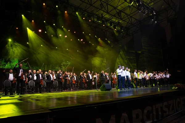 Az Örökség lángja koncert záróképe a teljes színpaddal, a két zenekarral és a tapsoló margitszigeti közönséggel.