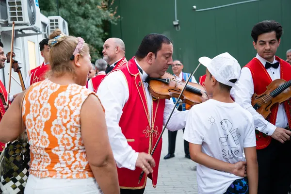 Egy SUGO-pólós fiú beszélget a 100 Tagú Cigányzenekar hegedűsével a margitszigeti főpróba előtt.