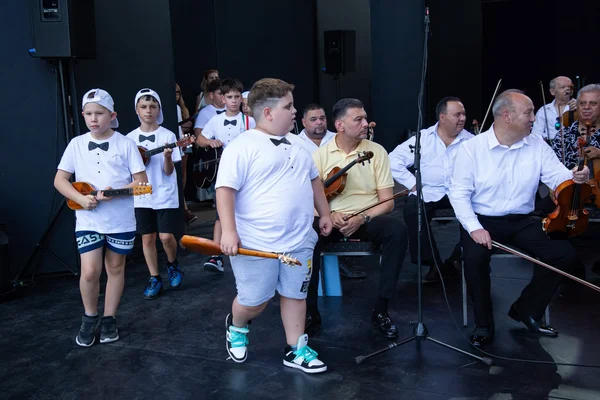 A SUGO fiatal muzsikusai hangszerekkel várnak a főpróbán, mellettük ülve készülnek a nagyzenekar tagjai.