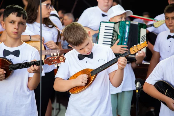 Egy fiatal tamburás összpontosít játék közben a főpróbán, mögötte harmonikás és további zenésztársak láthatók.