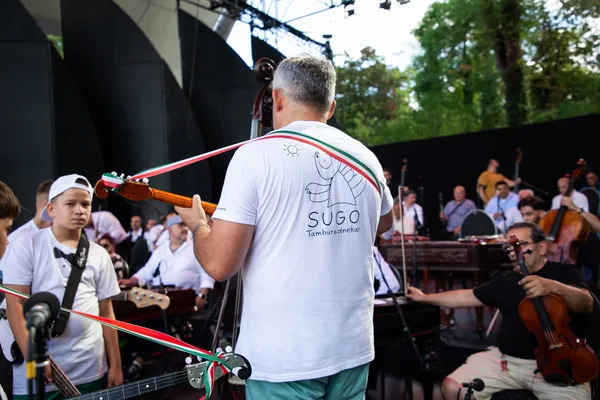 Nébl Zsolt hátulról, SUGO feliratú pólóban játszik a főpróbán, szemben a fiatal zenekari tagokkal.