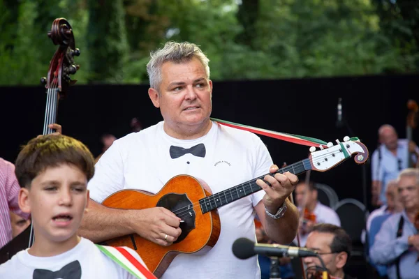Nébl Zsolt a főpróbán játszik, előtérben egy fiatal énekes látható, háttérben a kísérő zenekar tagjaival.